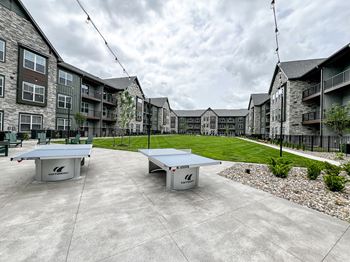 an outdoor patio with two ping pong tables in front of an apartment building at The Depot, Raymore, Missouri